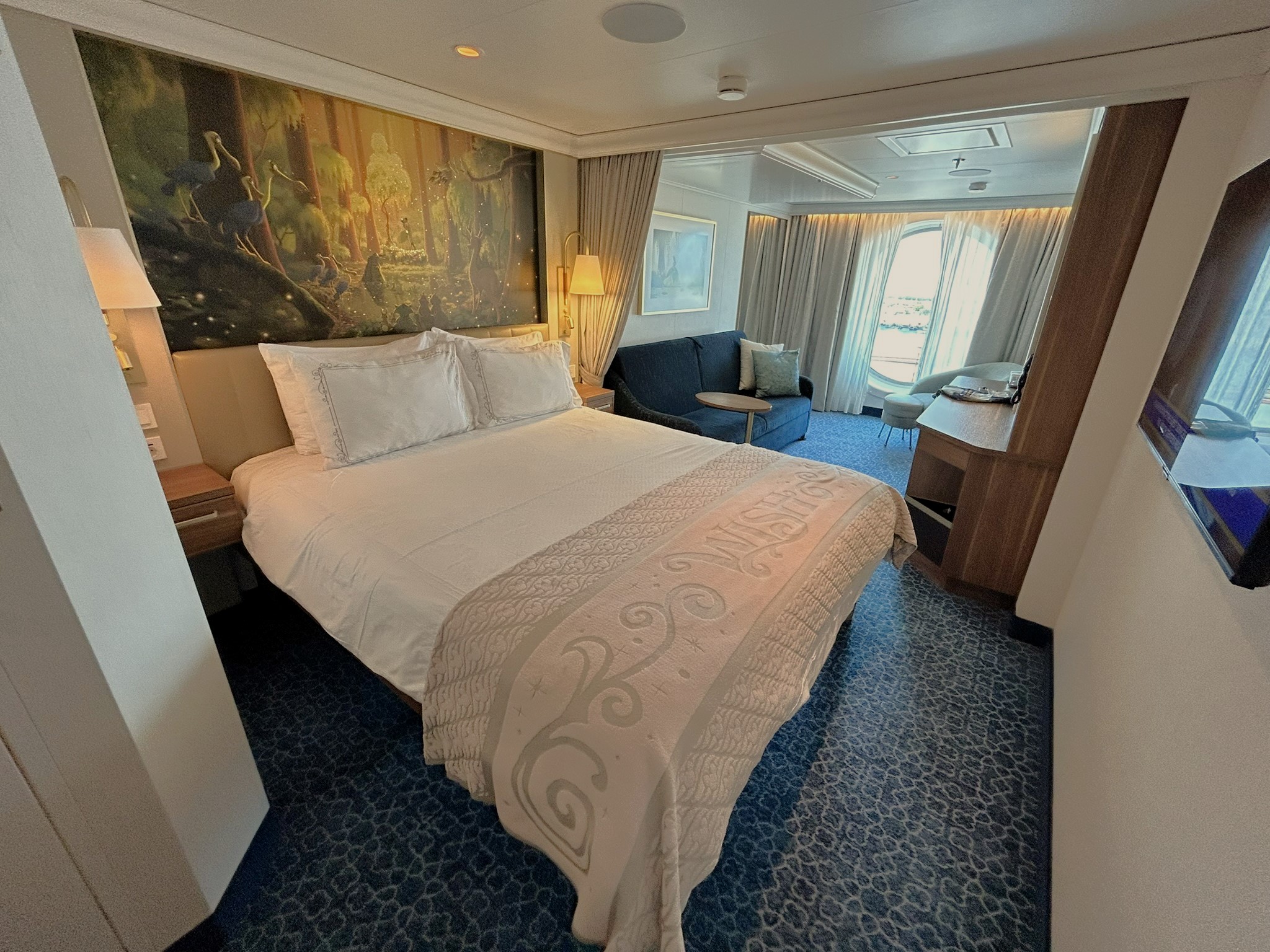 A tidy stateroom aboard a Disney cruise ship with a made bed and porthole